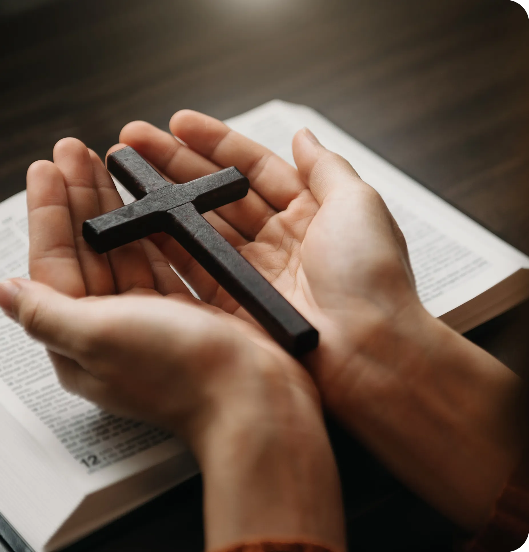 Hands holding a cross over open book.